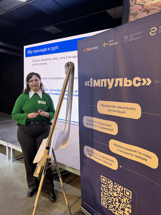 На цій фотографії зображена фасилітаторка заходу Тетяна Воскобойнікова - виконавча директорка громадської організації Спільно Hub, та банер наших грантодавців.